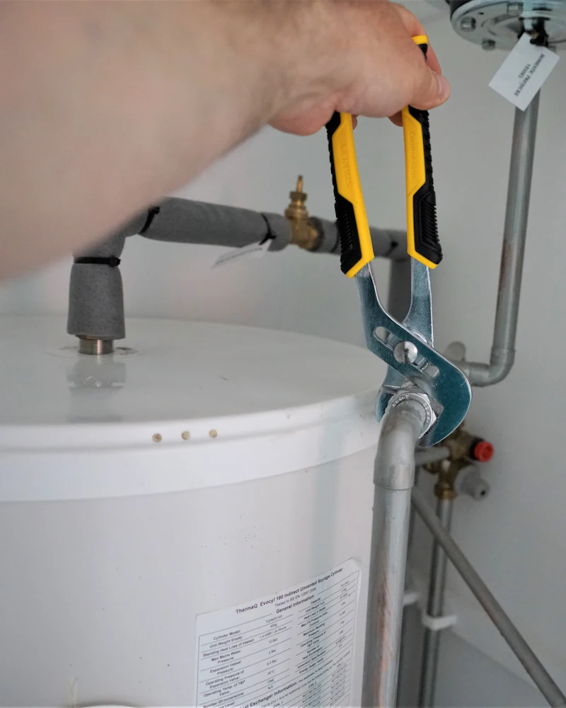 Plomero ajustando con una pinza la conexión de agua de un termotanque